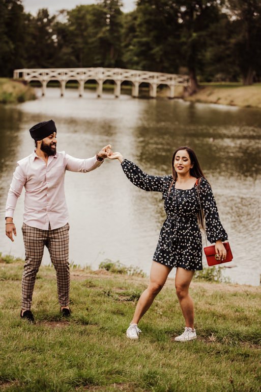 Couple holding hands near a river at the Painshill Park Surrey engagement shoot