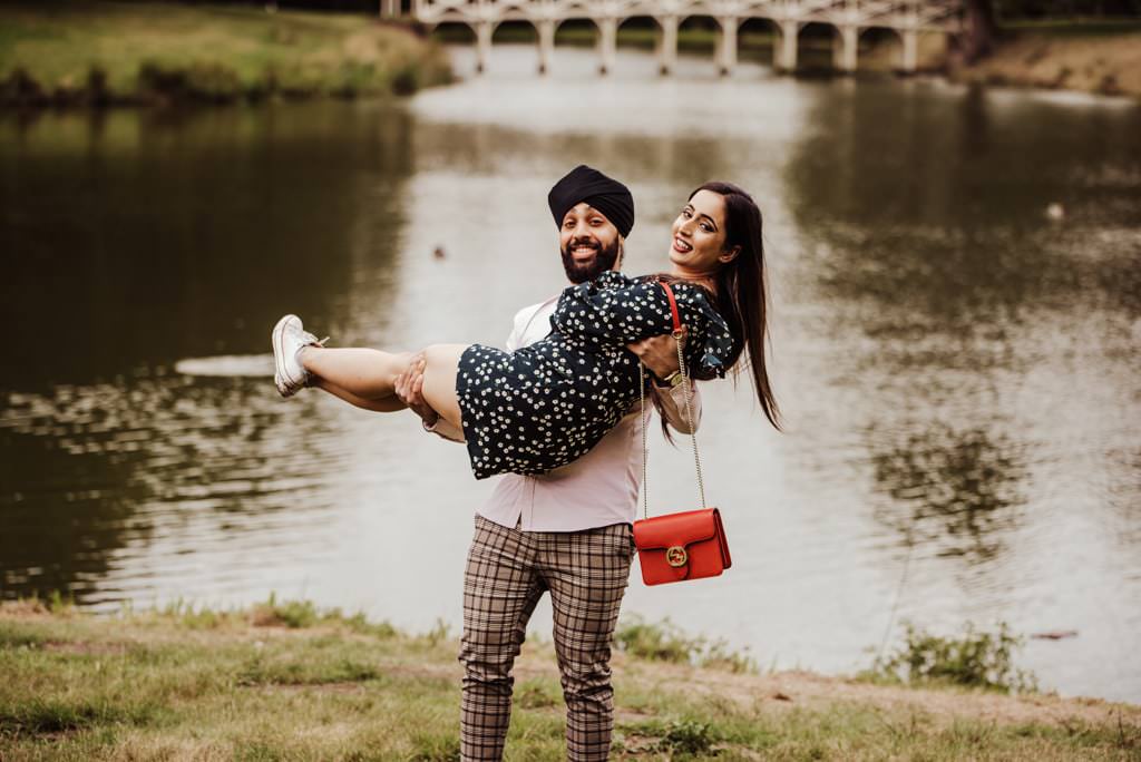 Fiance picking up his fiancé near a river at the Painshill Park Surrey engagement shoot