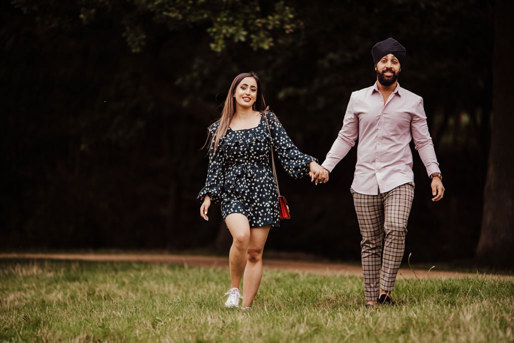Couple holding hands and walking near a river at the Painshill Park Surrey engagement shoot