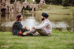Couple sitting down and giggling near a river at the Painshill Park Surrey engagement shoot