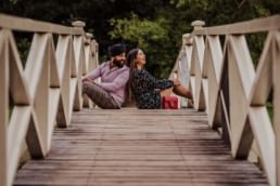 Couple sitting on the bridge and laughing near a river at the Painshill Park Surrey engagement shoot