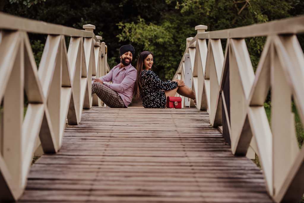 Couple sitting on the bridge near a river at the Painshill Park Surrey engagement shoot
