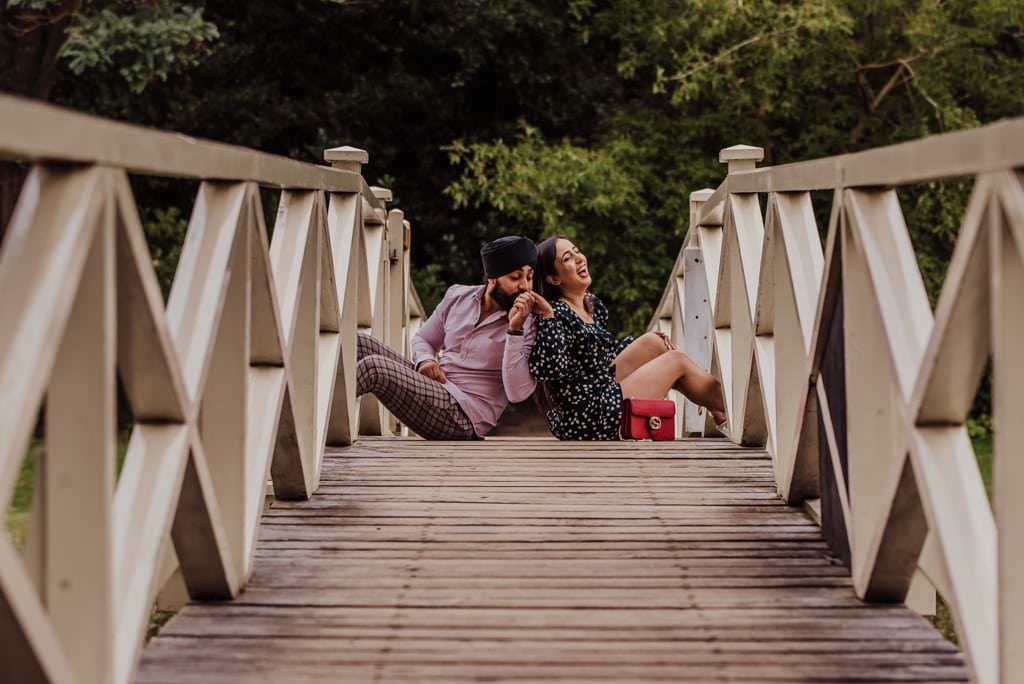 Couple sitting on the bridge near a river at the Painshill Park Surrey engagement shoot