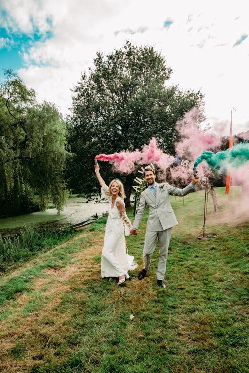 Bride and groom with colorful smoke bomds walking towards the photogrpaher in the filred decorated with tipi and festival ballons