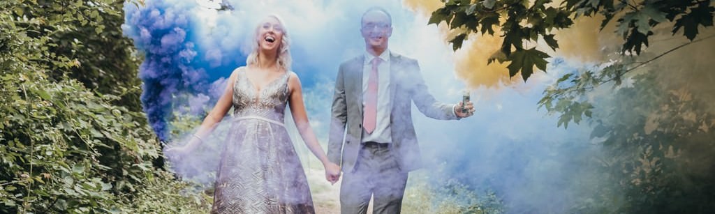 Bride and groom wearing wedding outfits with smoke grenades in the hand laughin
