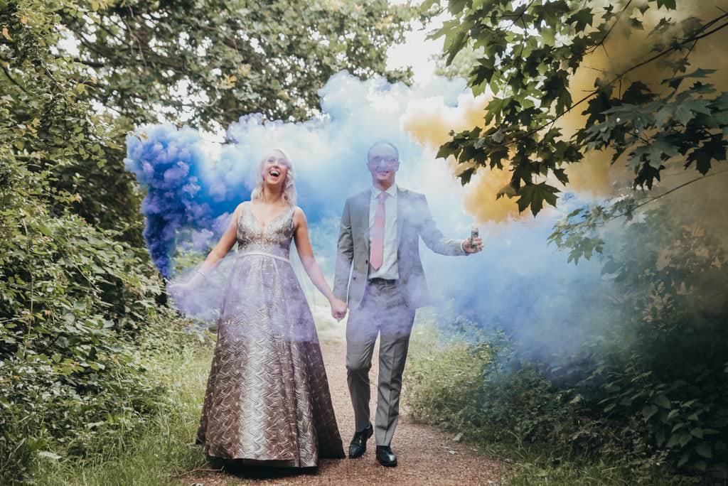 Bride and groom wearing wedding outfits with smoke grenades in the hand laughin