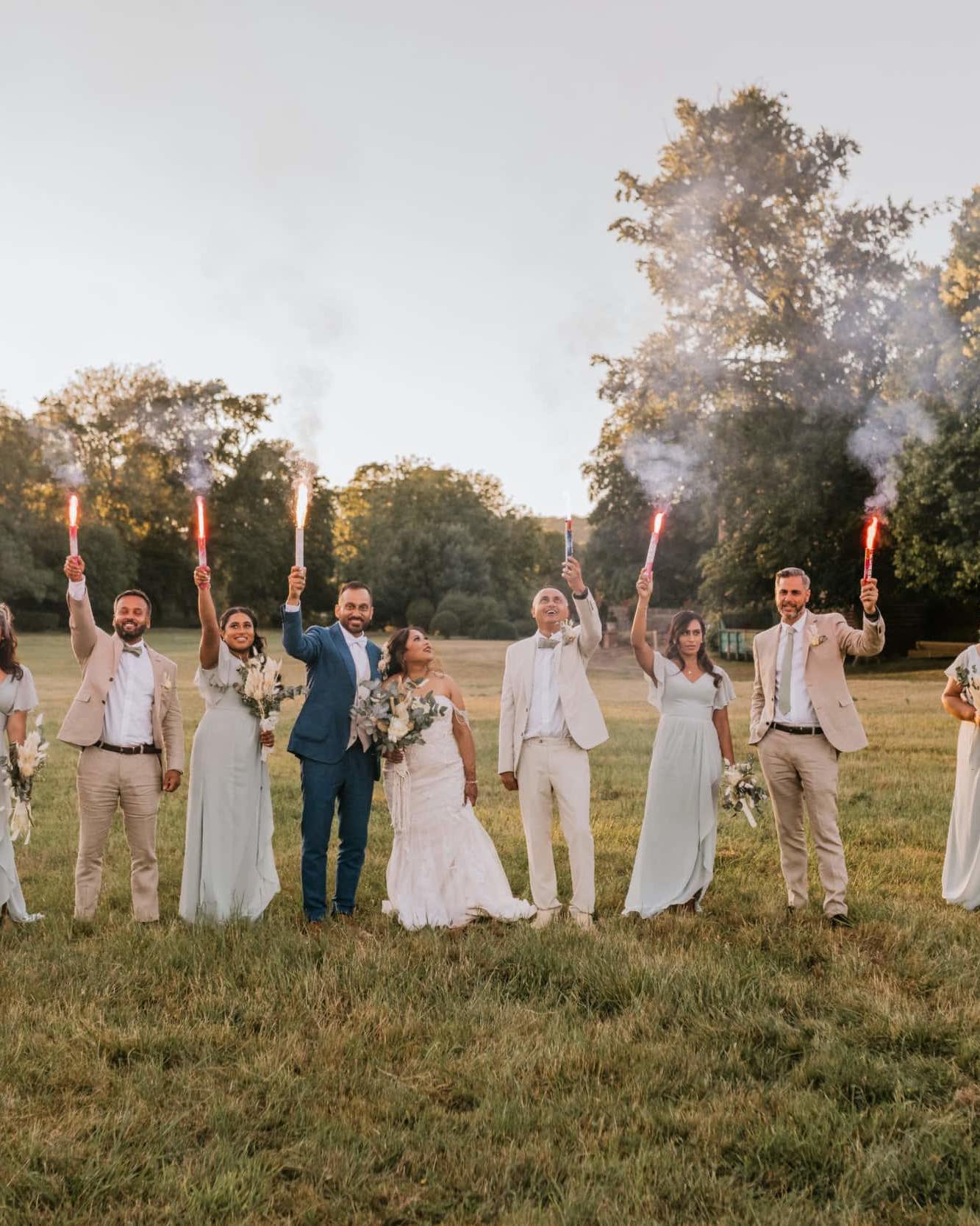 Groomsman, bridesmaids and couple walking towards the camera with sparklers in their hand