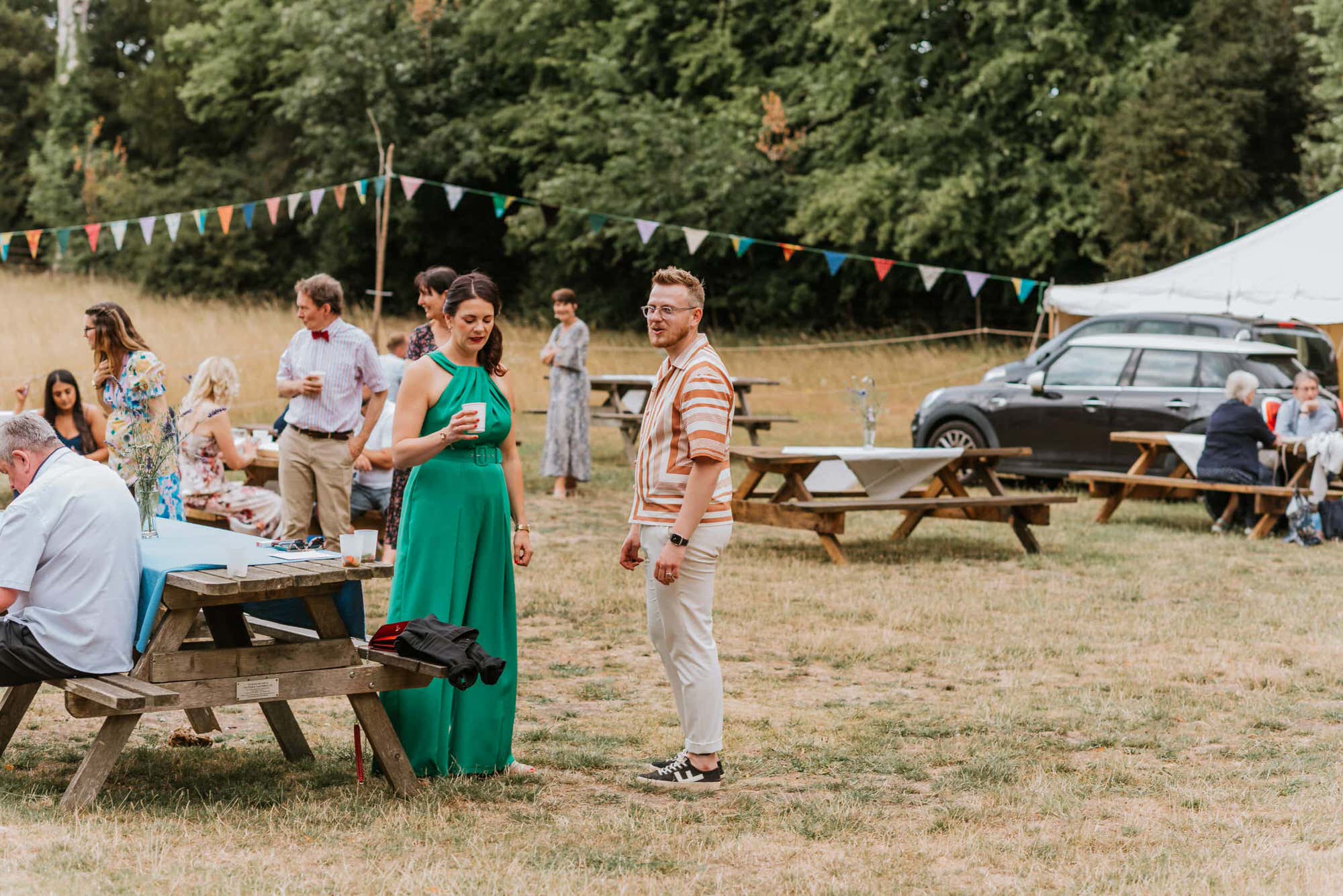 groom talking to a lady in green dress, bunting decorations and pub benches